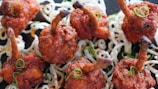Crispy, fried chicken skewers arranged on a bed of white, curly, fried noodles, garnished with thinly sliced green onions.