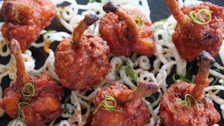 Crispy, fried chicken skewers arranged on a bed of white, curly, fried noodles, garnished with thinly sliced green onions.