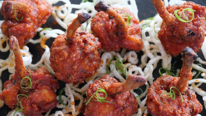 Crispy, fried chicken skewers arranged on a bed of white, curly, fried noodles, garnished with thinly sliced green onions.