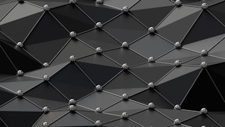An abstract geometric pattern featuring interconnected polygons with metallic spheres at each vertex. The polygons are three-dimensional triangles and quadrilaterals creating a tiled effect. The overall design has a sleek and modern aesthetic.