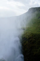 A misty waterfall framed by rugged cliffs under a cloudy sky.