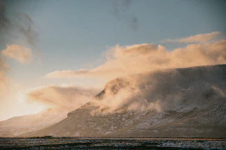 A dreamy mountain landscape with soft clouds and warm sunlight filtering through.