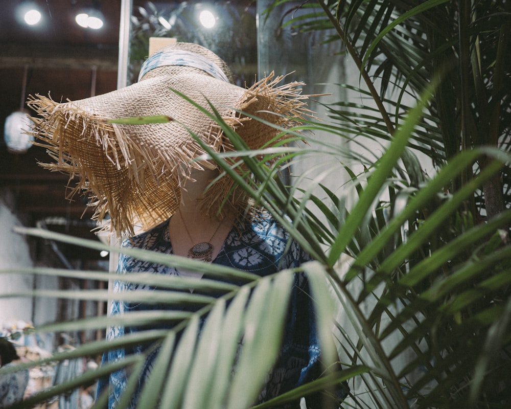 a woman wearing a straw hat standing next to a palm tree