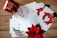 A collection of holiday greeting cards is spread out on a wooden surface. The cards feature festive designs, including red mittens holding a heart-shaped snowball and golden leaves. A red mug with winter-themed illustrations and a poinsettia plant add a seasonal touch.