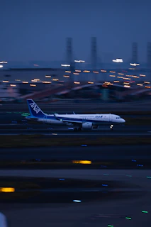 A sleek airplane taking off at dusk with city lights below.
