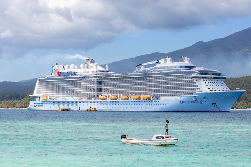 a man standing on a small boat in the water next to a large cruise ship