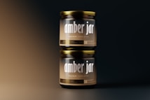Two amber glass jars stacked vertically against a gradient background. The jars have metallic lids and labels displaying the text 'amber jar' and 'mockup templates' in bold typography. The lighting creates a soft, warm glow on the jars, highlighting their glossy surface.