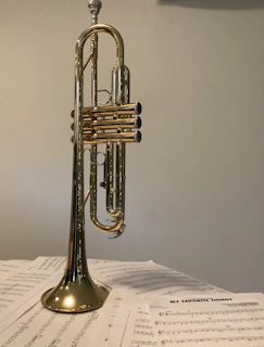 Brass band sheet music stacked neatly next to a trumpet and a pair of music glasses.