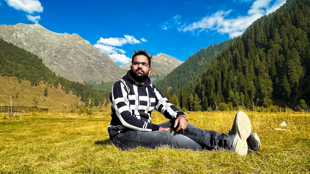 a man sitting in a field with mountains in the background