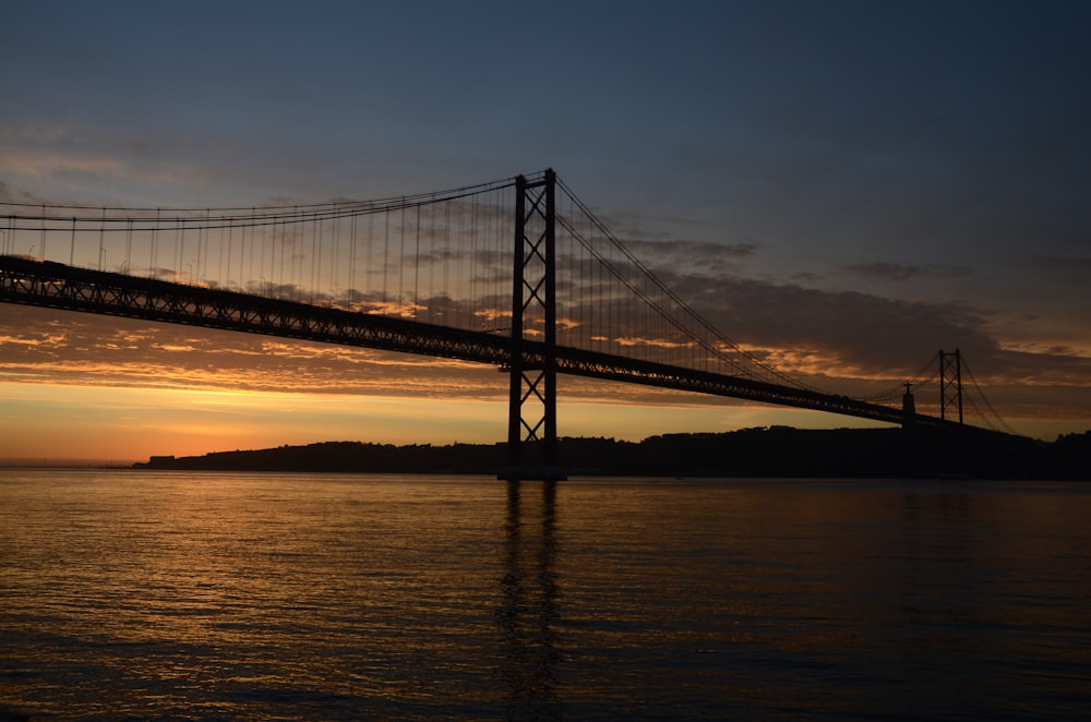 the sun is setting behind a bridge over the water