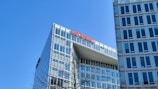 A modern office building with extensive glass windows under a clear blue sky. The red lettering at the top reads 'DER SPIEGEL', indicating the building's association. Nearby, leafless tree branches partially obscure the view.