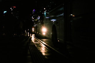 A sleek modern bus driving on a dark road at dusk with city lights in the background.