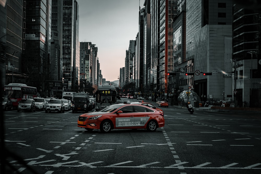 a red car driving down a street next to tall buildings