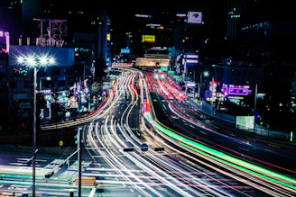 A vibrant time-lapse photo of a bustling city street glowing with neon lights.
