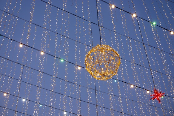 A decorative setup featuring numerous strings of small, twinkling lights hanging vertically against the evening sky. A large, illuminated spherical figure made of lights is prominently displayed, along with a red star-shaped decoration.