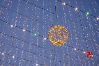 A decorative setup featuring numerous strings of small, twinkling lights hanging vertically against the evening sky. A large, illuminated spherical figure made of lights is prominently displayed, along with a red star-shaped decoration.