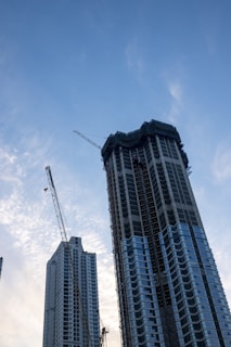 A modern skyscraper under construction with cranes in the background.