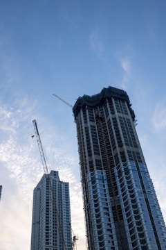 Modern skyscraper under construction with scaffolding and cranes.