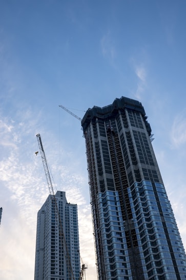 A modern skyscraper under construction with cranes in the background.