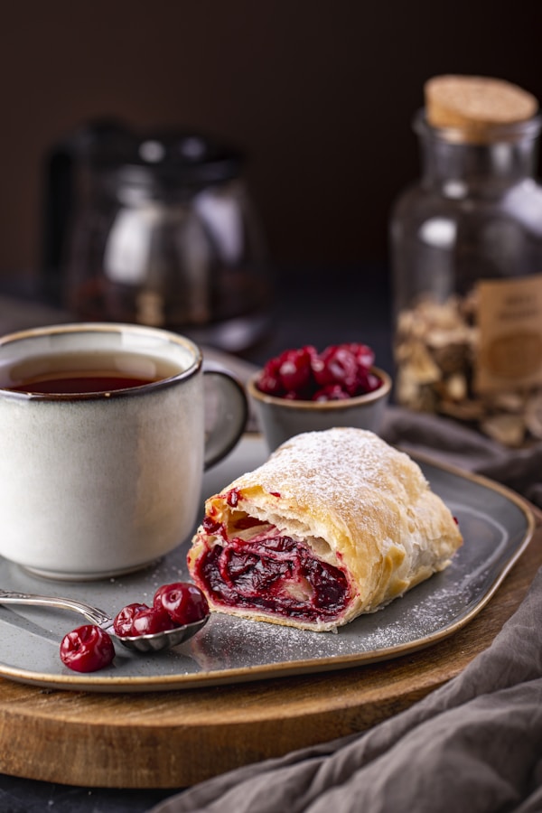 A cranberry filled pastry on a plate next to a cup of tea