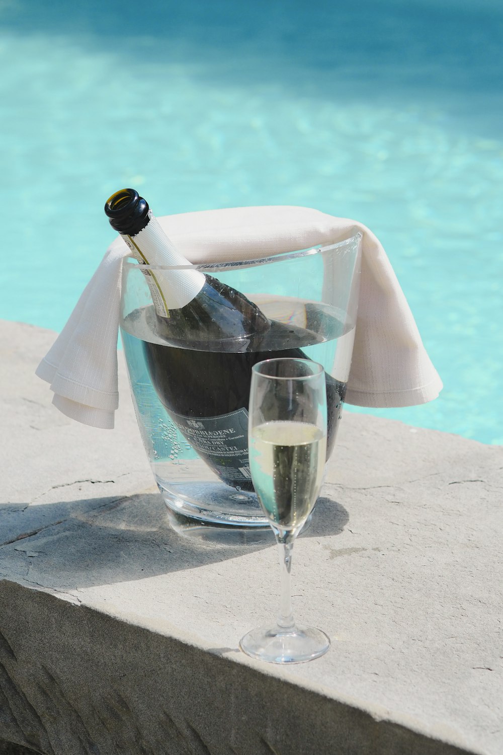 a bottle of wine and a glass of wine on a ledge near a pool