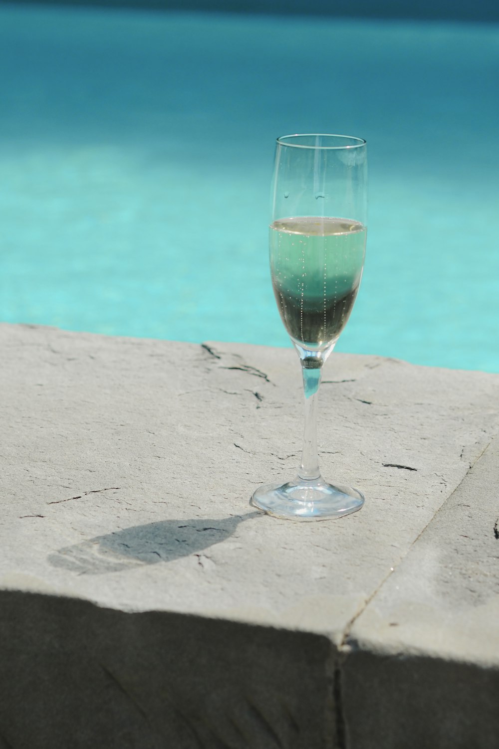 a glass of wine sitting next to a swimming pool