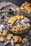 An assortment of pastries and cookies is artfully arranged on a dark textured surface. A mix of powdered sugar-coated confections, buttery cookies, and intricate designs are present. A cup of black coffee sits in a greenish cup and saucer, adding a contrasting element to the image. The scene evokes an inviting and cozy atmosphere.