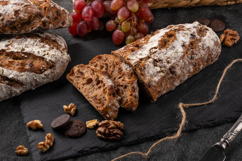 a loaf of bread, nuts, and grapes on a slate board