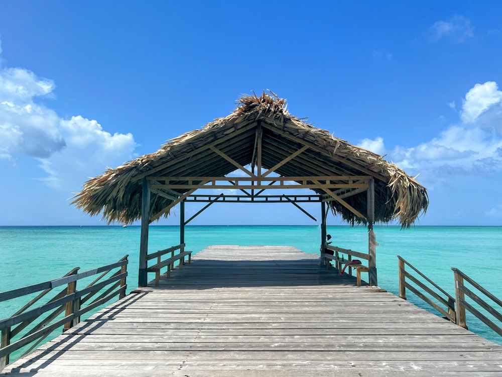 a wooden pier with a thatched roof over the ocean
