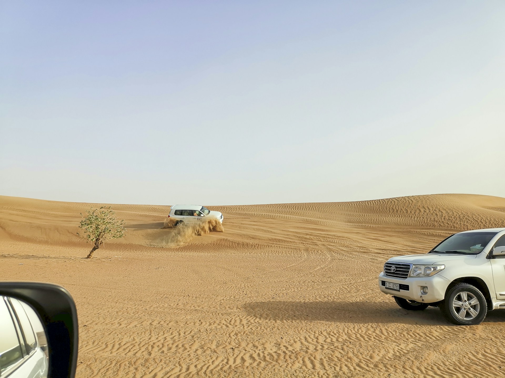 a car driving through the desert with a truck in the background