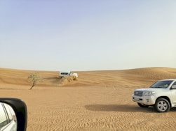 a car driving through the desert with a truck in the background