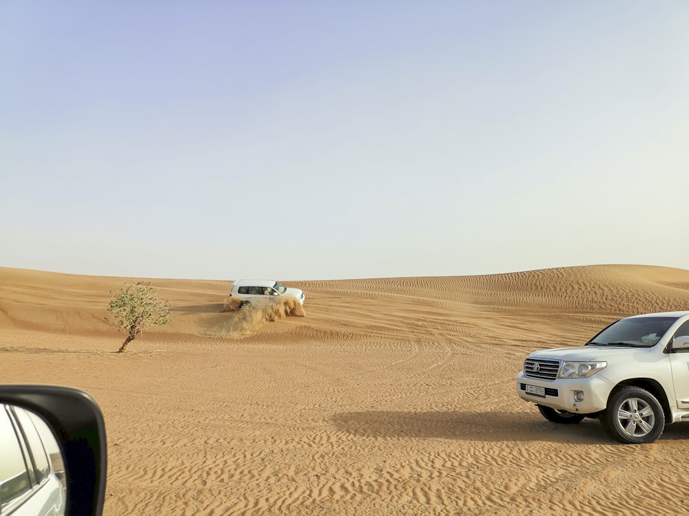 a car driving through the desert with a truck in the background