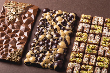 Artisan chocolate bars arranged on a wooden board, showcasing a variety of flavors with nuts and spices.