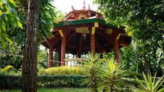 A cozy gazebo made from polished teak wood surrounded by tropical plants.