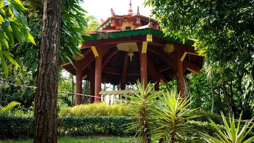 Cozy gazebo made from polished teak wood surrounded by tropical plants.