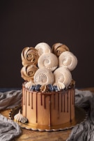 A beautifully decorated cake with rich chocolate layers, topped with artful meringue swirls resembling roses. Accented with fresh blueberries and small silver beads, the cake features a glossy chocolate drip down its sides. It sits on a wooden surface with a dark backdrop, enhancing its elegant aesthetic.