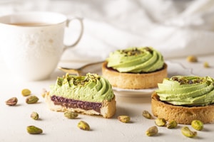 A warm, inviting setting showing a cup of pistachio coffee next to scattered green Antep pistachios on a softly lit beige background.