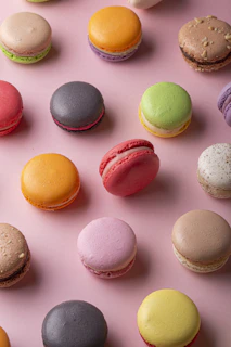 Brightly colored macarons arranged in a neat row on a pastel pink background.