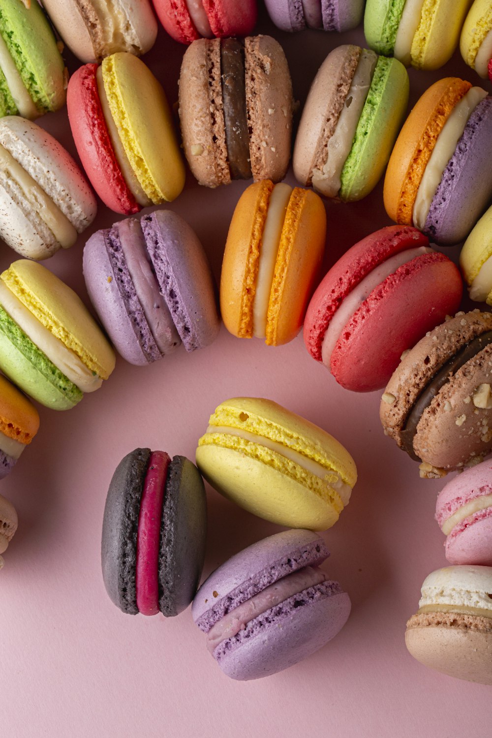 a bunch of different colored macaroons on a pink surface