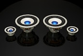 Four speaker subwoofers with blue center domes are arranged symmetrically against a black background, showcasing different sizes from left to right. The speakers have a metallic frame with black rubber surrounds and reflect light subtly, adding depth to the image.