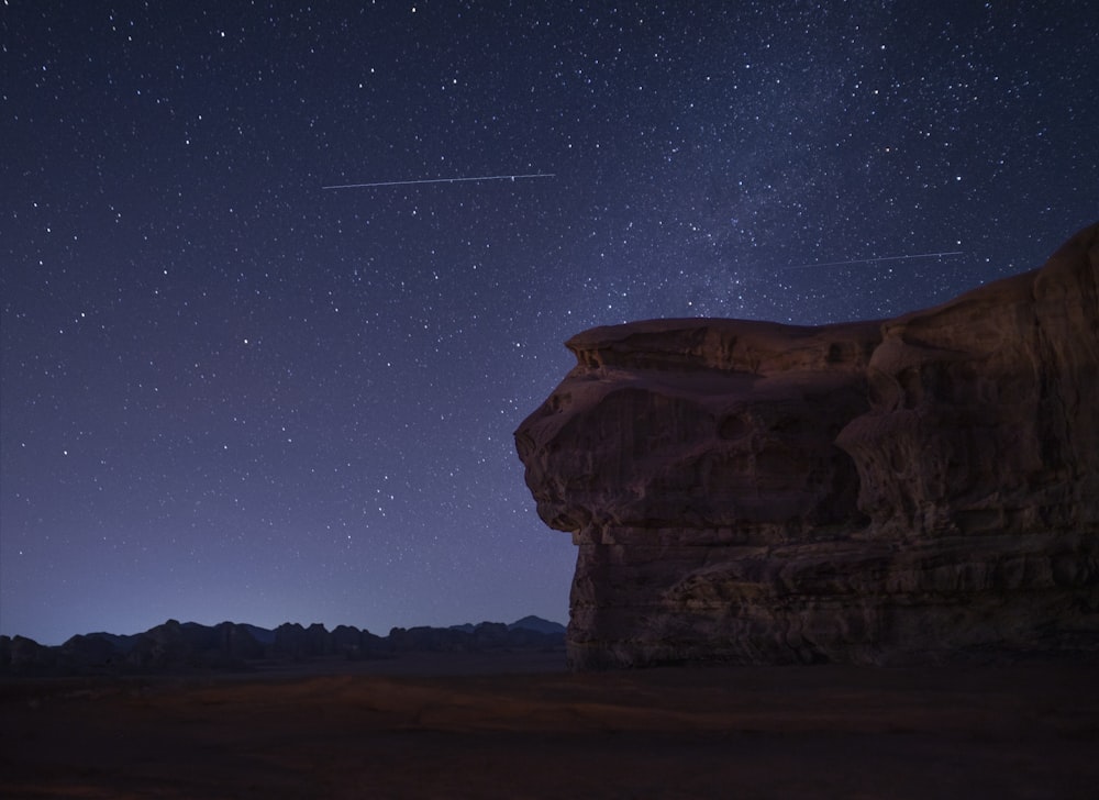 the night sky with stars above a rocky outcropping