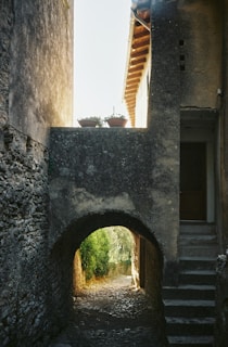 An old cobblestone alley leading towards an ancient stone archway bathed in warm afternoon sun.