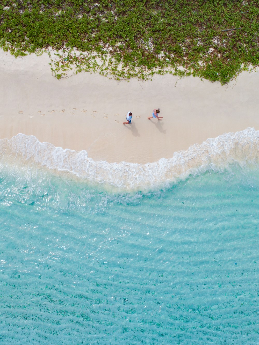 two people walking on a beach next to the ocean