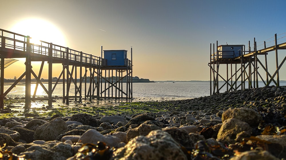 the sun is setting over the water near a pier