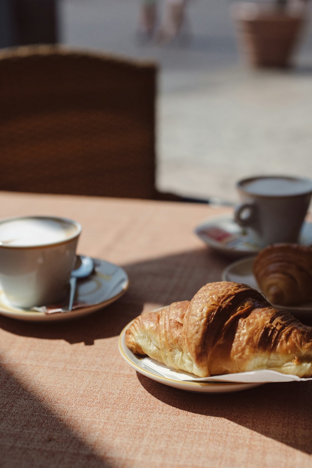Un croissant se coloca en un plato junto a una taza de café