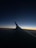 A darkened view showing an airplane wing with a gradient sky transitioning from deep blue to orange at the horizon, indicating either sunrise or sunset.