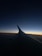 A darkened view showing an airplane wing with a gradient sky transitioning from deep blue to orange at the horizon, indicating either sunrise or sunset.