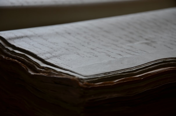 An old, thick stack of handwritten documents with visible texture and slight yellowing of the pages. The focus is on the edges, highlighting the layered, slightly curled paper.