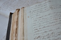 An ancient, weathered book lying open on a wooden table with quill and ink beside it.