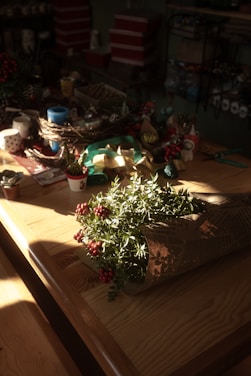 A sunlit wooden table scattered with colorful craft supplies and a small potted plant.